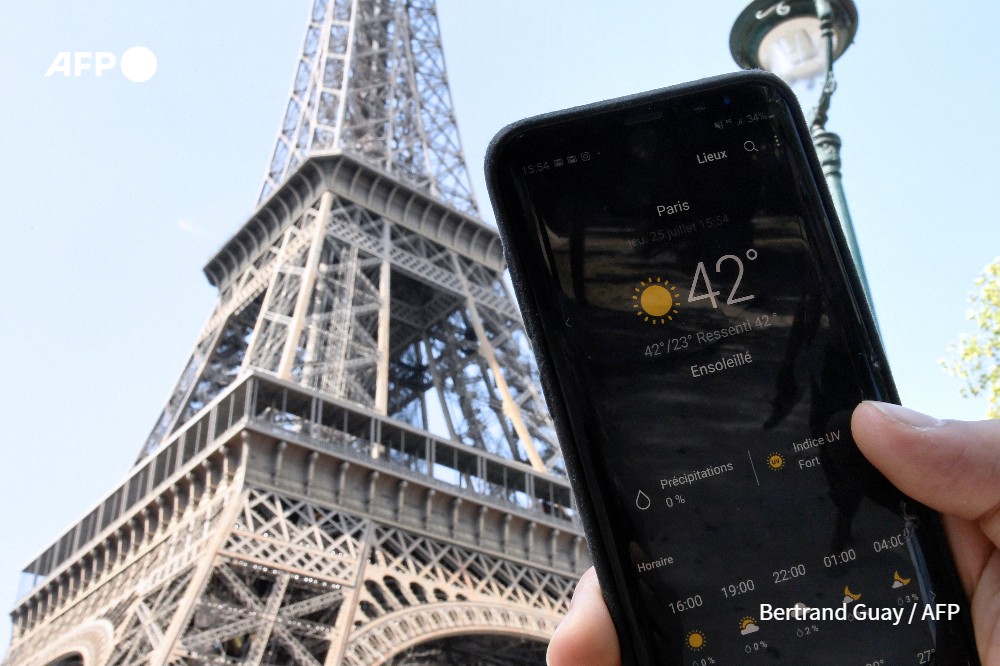 Une personne se tenant à côté de la Tour Eiffel tient un smartphone indiquant une température de 42 degrés Celsius, le 25 juillet 2019 à Paris, alors qu'une nouvelle vague de chaleur frappe la capitale française. - AFP