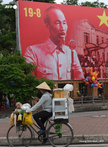 Une vendeuse des rues passe devant un panneau représentant Ho Chi Minh, le Père de l'indépendance du Vietnam Hoang Dinh Nam - AFP