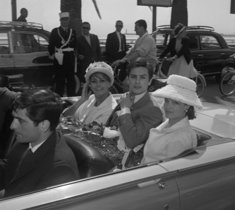 Alain Delon, entouré de Sophia Loren (G) et Romy Schneider (D) arrive en décapotable devant le Palais des festivals, le 8 mai 1962 - AFP